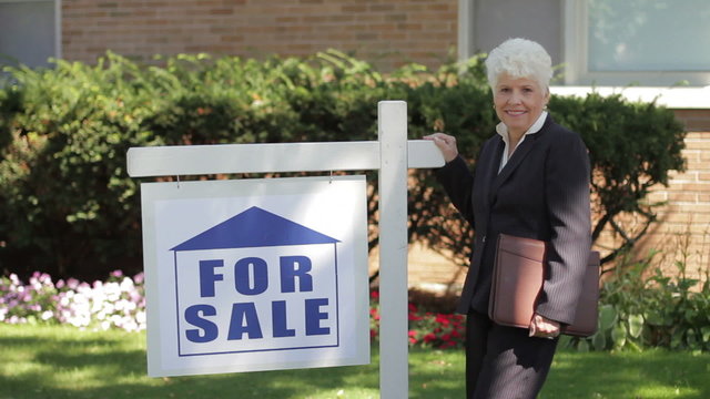Real estate agent in front of house by for sale sign