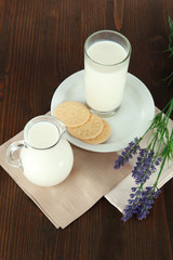 Glass of milk, a jug and cookies on a wooden background