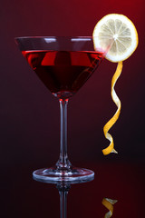 Red cocktail in martini glass on dark red background