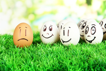 Eggs with funny faces on grass on bright background