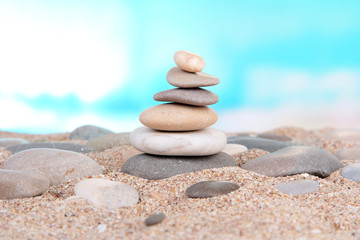 Fototapeta na wymiar Tower of sea stones on sand on bright background