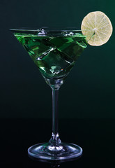 Green cocktail with lime on dark green background