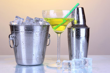 Metal ice bucket and shaker and cocktail on yellow background