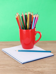 Obraz premium Colorful pencils in cup on table on green background