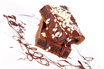 Slices of a brownie on white coverd with chocolate and nuts