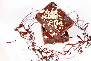 Slices of a brownie on white coverd with chocolate and nuts