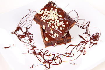 Slices of a brownie on white coverd with chocolate and nuts