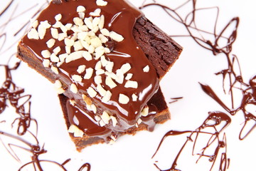 Slices of a brownie on white coverd with chocolate and nuts