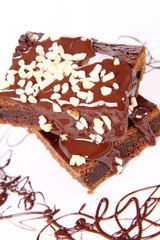 Slices of a brownie on a plate covered with chocolate and nuts