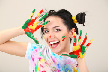 Young pretty painter with hands in paint, on gray background