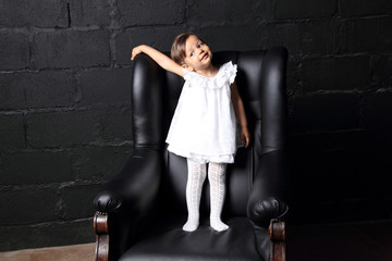 The child in a white dress is on a black chair