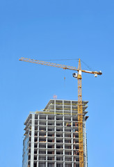 Building crane and building under construction against blue sky