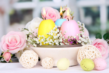 Easter candles with flowers on window background