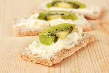Tasty canapes with cheese and kiwi, on wooden background
