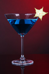 Blue cocktail in martini glass on dark red background
