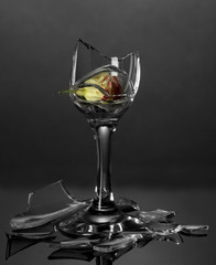 Broken wineglass with dry flower on grey background