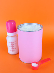 Powdered milk with baby bottle of milk on orange background