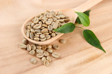 Green coffee beans in spoon and leaves on wooden background