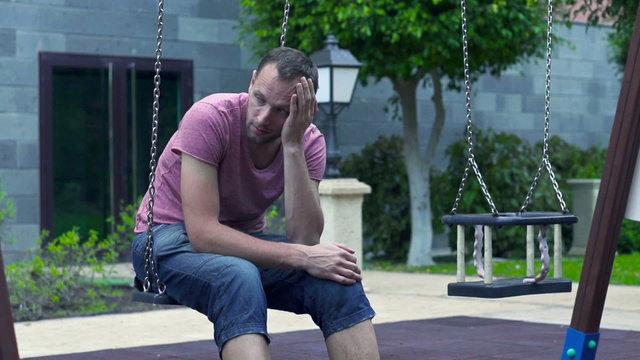 Sad man sitting on a swing, slow motion shot at 60fps 