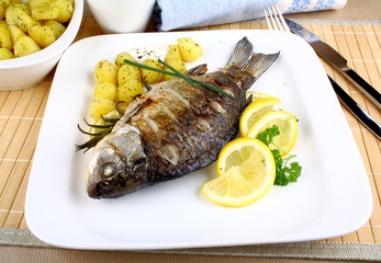 Grilled fish with potatoes, sauce, lemon and cutlery
