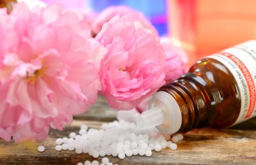 Globuli mit Kirschblüten auf Holz mit Flasche