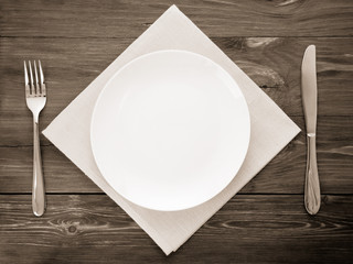 white plate, knife and fork on wood