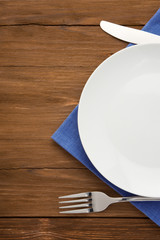 white plate, knife and fork on wood