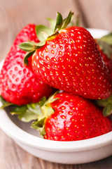 Close-up of strawberries in white plate on wooden table. 