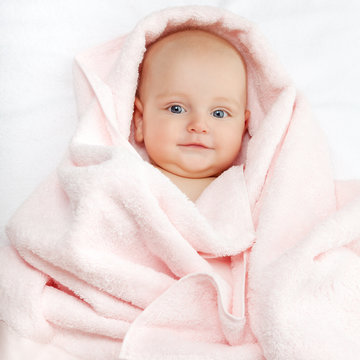 Caucasian baby boy covered with pink towel joyfully smiles at ca