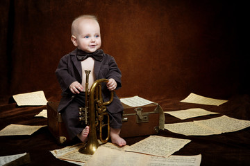 Caucasian baby boy plays with trumpet between sheets with musica