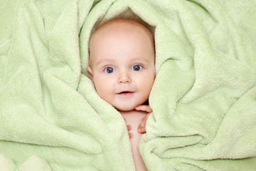 Caucasian baby boy covered with green towel joyfully smiles at c