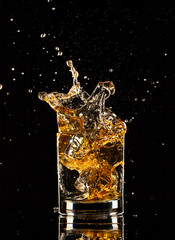 Whiskey splashing out of glass on black background