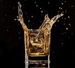 Whiskey splashing out of glass on black background