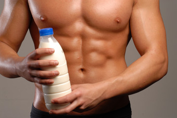 Hombre sano y musculoso sujetando una botella de leche.