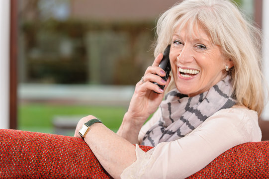 Gl&uuml;ckliche Seniorin telefoniert auf dem Sofa