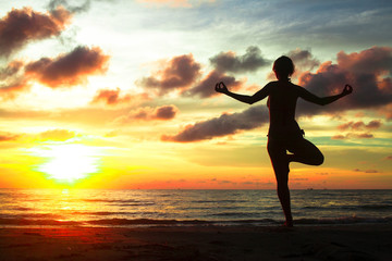 Fototapeta na wymiar Young woman practicing yoga on the beach during sunset.