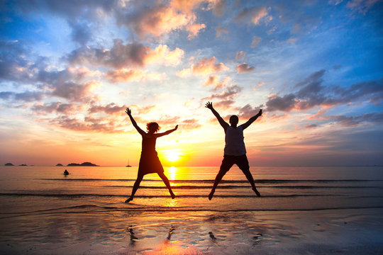 Young couple in a jump on the sea beach at sunset