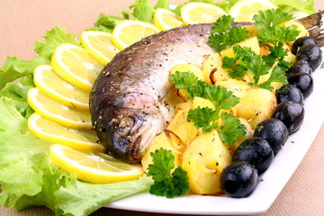 Baked trout with potatoes, black olives, salad and lemon