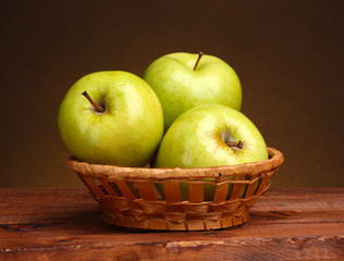 juicy green apples in basket on wooden table on brown