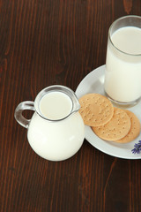 Glass of milk, a jug and cookies on a wooden background