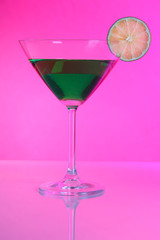 Green cocktail in martini glass on pink background