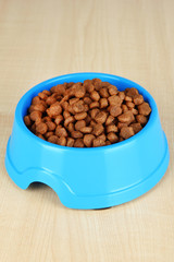 Dry dog food in bowl on wooden background