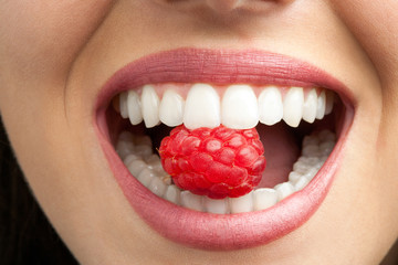 Perfect teeth biting raspberry. - obrazy, fototapety, plakaty