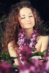 Beautiful woman on a sunny day, sitting in the flowers of lilac 