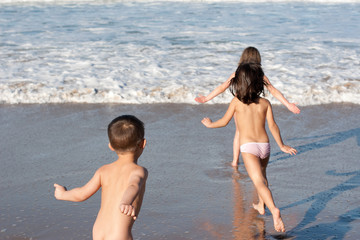 Three happy children running naked into the waves