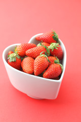 Strawberry in heart shape bowl on red background