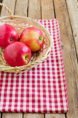 Red apples in basket on tablecloth over wooden background