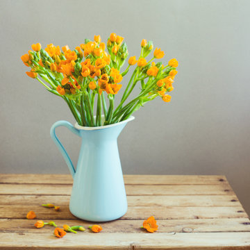 Orange Flowers In Blue Jug On Wooden Table