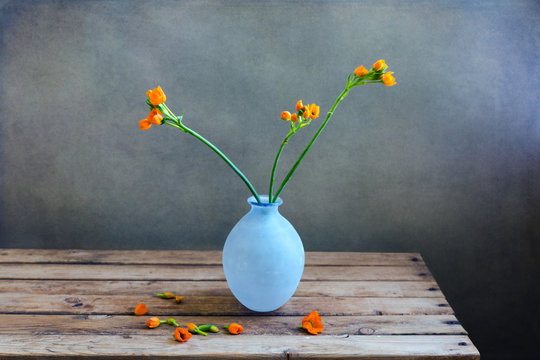Orange Flowers In Blue Vase On Wooden Deck Table