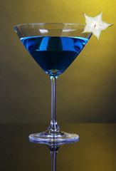 Blue cocktail in martini glass on dark yellow background